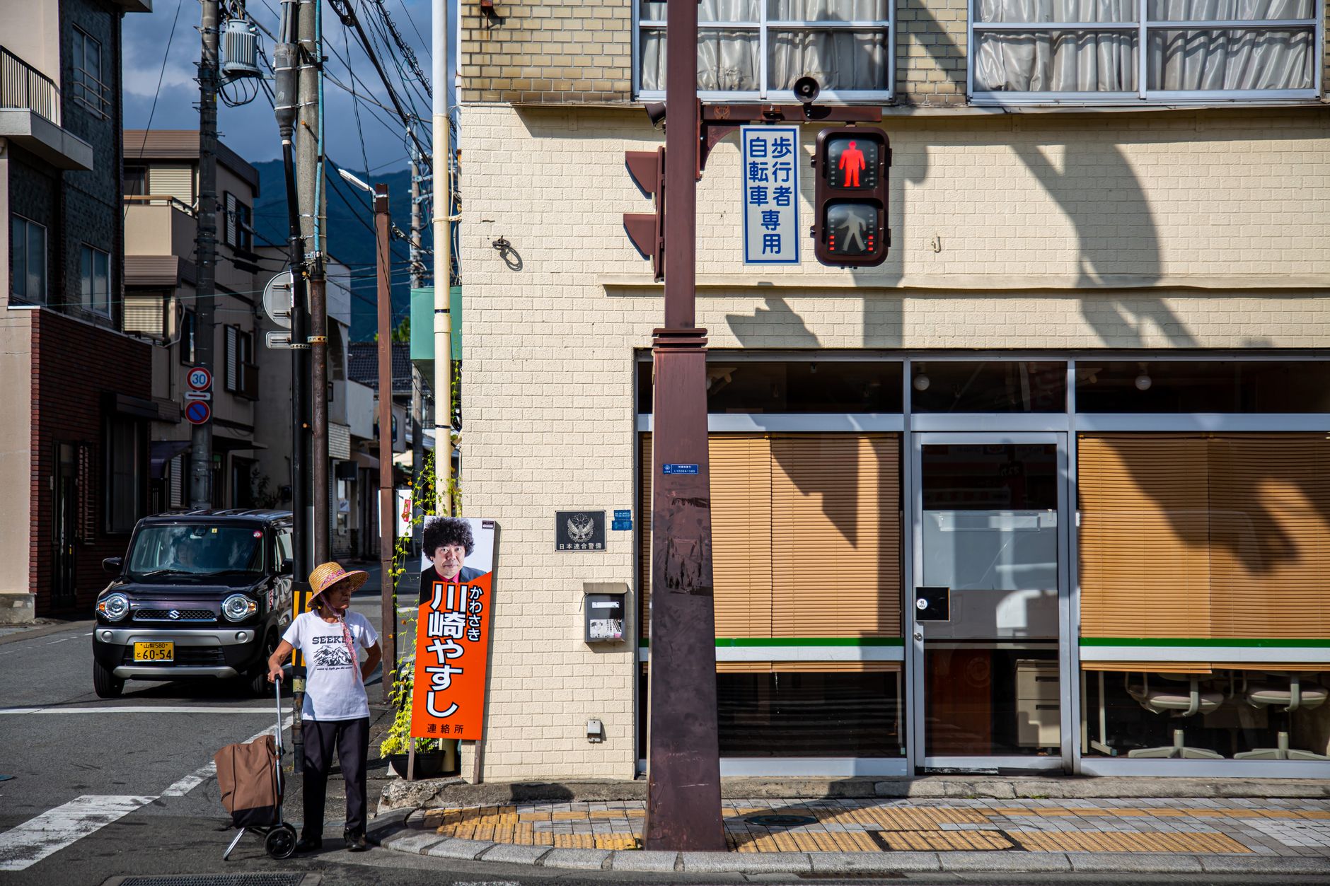 Street view in Nagano City, featuring a person waiting at a crosswalk under a traffic light.